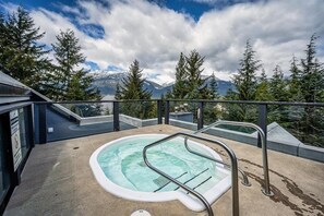 Ein Whirlpool mit Metallleiter, umgeben von einer Betonplattform, mit Blick auf Berge und Bäume im Hintergrund.