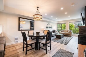 A spacious living room with a dining area, large windows, and a fireplace. - Walk to Blackcomb | Complex hot tub | BBQ (Whistler)