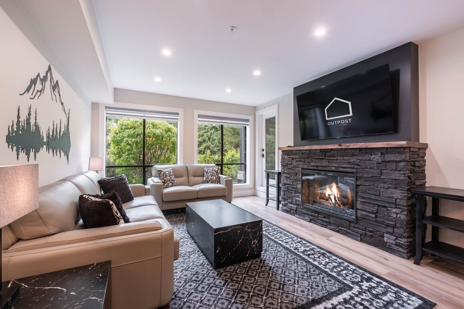 A modern living room with a fireplace, leather sofas, a flat-screen TV, and large windows.