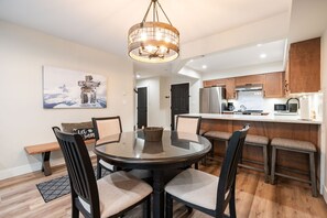 A modern kitchen with wooden cabinets, a stainless steel refrigerator, and a dining area with a round table and chairs. - Walk to Blackcomb | Complex hot tub | BBQ (Whistler)