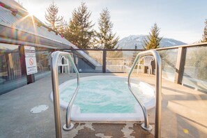 An outdoor hot tub with metal railings, surrounded by a glass enclosure, with a view of trees and mountains in the background. - Walk to Blackcomb | Complex hot tub | BBQ (Whistler)