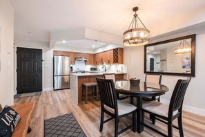 A modern kitchen with a central island, a dining area with a round table and chairs, and a large mirror on the wall. - Walk to Blackcomb | Complex hot tub | BBQ (Whistler)