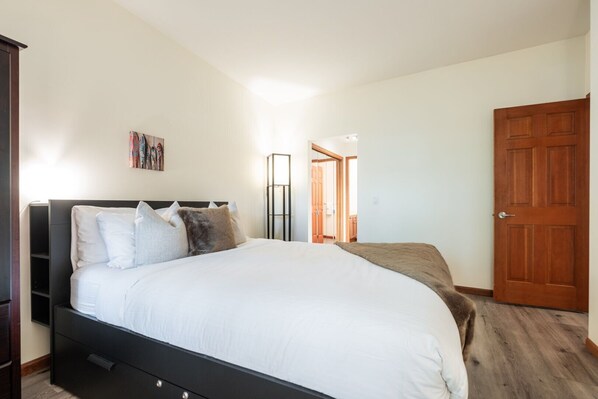 Ein Schlafzimmer mit einem großen Bett, einem Kleiderschrank, einer Tür und einem Flur, der in einen anderen Raum führt.
