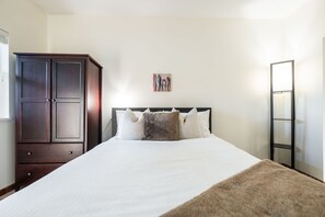 Ein Schlafzimmer mit einem großen Bett, einem Kleiderschrank, einem Gemälde an der Wand und einem hohen Spiegel.