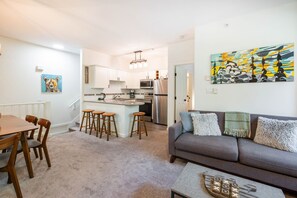 A modern kitchen with stainless steel appliances, a dining area with wooden chairs, and a gray sofa with decorative pillows. - Beautiful Condo | Shared hot tub | BBQ | Wifi (Whistler)