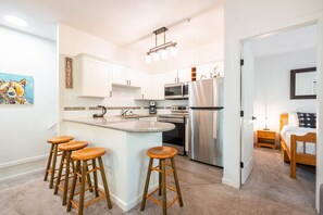 Een moderne keuken met witte kasten, een roestvrijstalen koelkast en een bar met krukken.