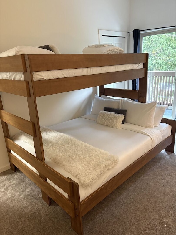 Una cama litera con un edredón blanco mullido y almohadas, un cabecero de madera, y vistas a la vegetación exterior.