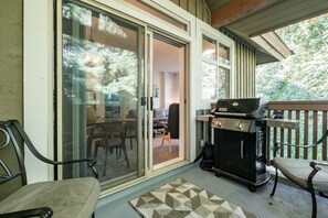 Een overdekt buitengebied met een barbecue, schuiframen en een eettafel met stoelen.