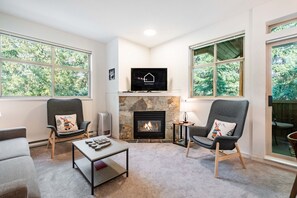 Een gezellige woonkamer met een open haard, twee fauteuils, een salontafel en een televisie.