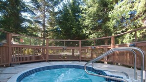 A hot tub with a metal ladder, surrounded by a wooden deck and trees. - Beautiful Condo | Shared hot tub | BBQ | Wifi (Whistler)