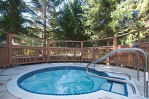 A hot tub with a metal ladder, surrounded by a wooden deck and trees. - Beautiful Condo | Shared hot tub | BBQ | Wifi (Whistler)
