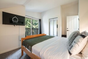 A bedroom with a bed, a television mounted on the wall, a window with a view of trees, and a door. - Beautiful Condo | Shared hot tub | BBQ | Wifi (Whistler)