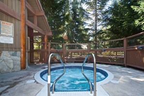 A hot tub area with a wooden deck and metal railings, surrounded by trees. - Beautiful Condo | Shared hot tub | BBQ | Wifi (Whistler)