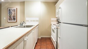 A kitchen with white cabinets, a stainless steel sink, a stove, and a refrigerator. - Ski-in/out apartment | Complex pool, hot tub & gym (Whistler)