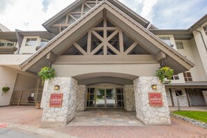 Ein Hotel mit steinverkleideter Fassade, einem hölzernen Vordach und zwei Schildern mit der Aufschrift 'The Aspens on Blackcomb'.
