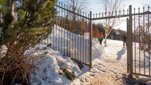 A snow-covered pathway with a metal gate, surrounded by trees and a clear sky. - Ski-in/out apartment | Complex pool, hot tub & gym (Whistler)
