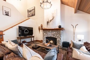 A cozy living room with a stone fireplace, a television, and a comfortable seating area. - Townhome | Private hot tub | BBQ | A/C | Pets (Whistler)