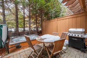 Un patio con un jacuzzi, una parrilla y sillas de madera.