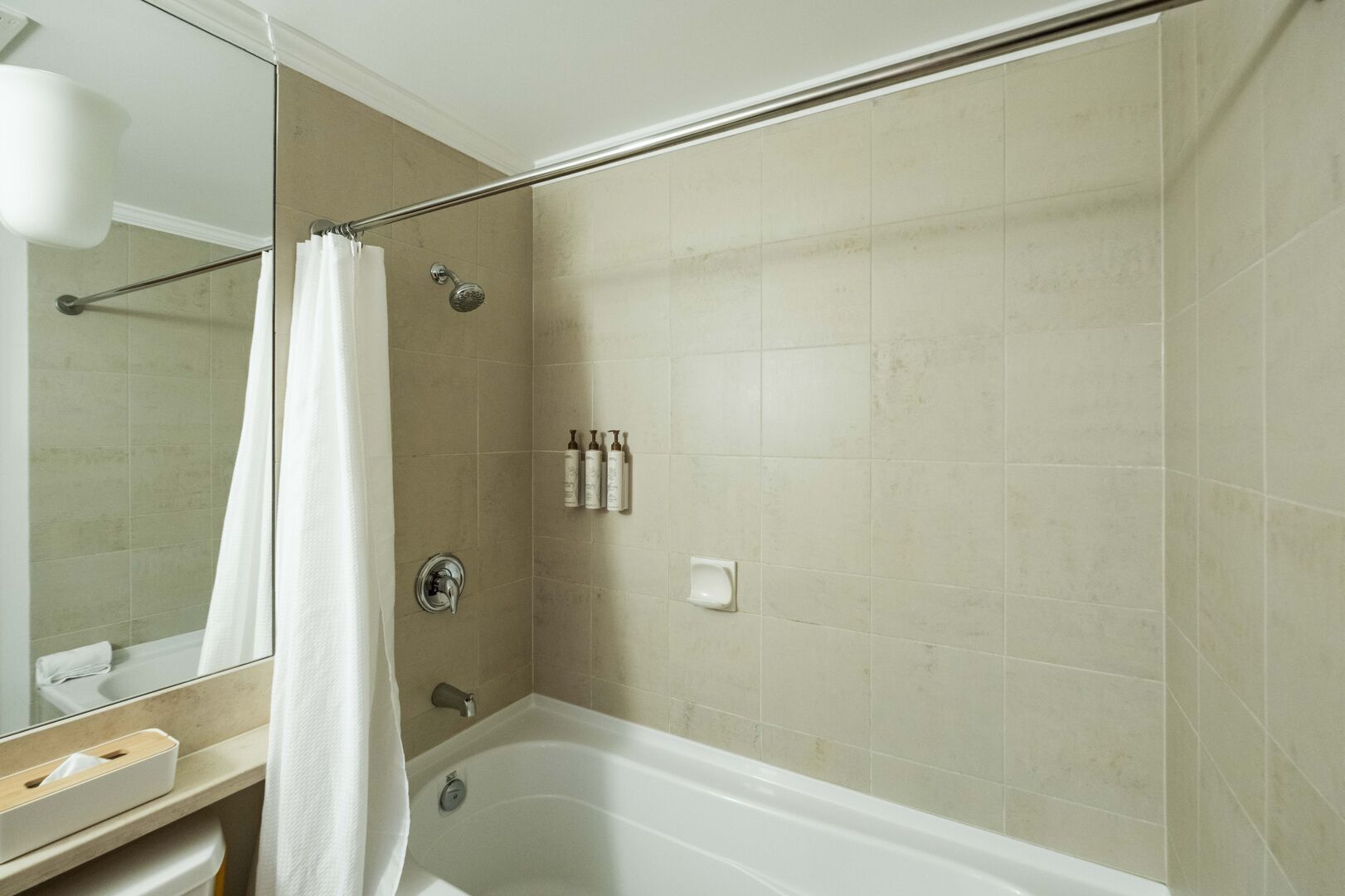 A bathroom with a bathtub, a shower, and a toilet. There are toiletries on the wall and a towel rack.