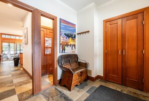 A hallway with a wooden bench, a poster of Whistler Village, and a set of wooden doors. - Townhome | Private hot tub | BBQ | A/C | Pets (Whistler)