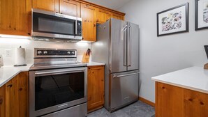 A modern kitchen with wooden cabinets, a stainless steel refrigerator, a microwave, and an oven. - Great location | Complex hot tub | BBQ | Smart TVs (Whistler)