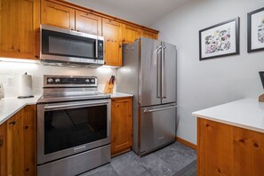 Eine moderne Küche mit Holzausstattung, einem Edelstahlkühlschrank, einer Mikrowelle und einem Backofen.