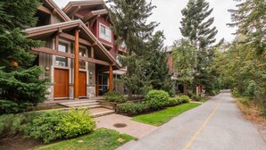 A two-story house with a front porch, wooden siding, and a driveway. - Great location | Complex hot tub | BBQ | Smart TVs (Whistler)