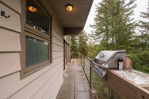 A covered outdoor area with a grill, a glass railing, and a wooden deck. - Luxury Home | Private hot tub | Pets | BBQ | AC (Whistler)