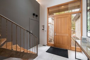 Un interno moderno con una scala in legno, una porta vetrata che dà sull'esterno e una piccola area esterna visibile attraverso la porta.