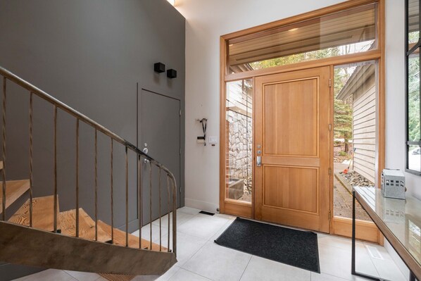 Un interior modern amb una escala de fusta, una porta de vidre que dona a l'exterior i una petita zona exterior visible a través de la porta.