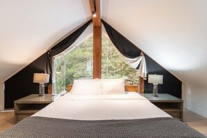 Una camera da letto con un letto grande, due comodini con lampade e vista sugli alberi dalla finestra.