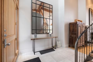 A hallway with a wooden door, a console table with a mirror, a staircase, and a sign on the floor. - Luxury Home | Private hot tub | Pets | BBQ | AC (Whistler)