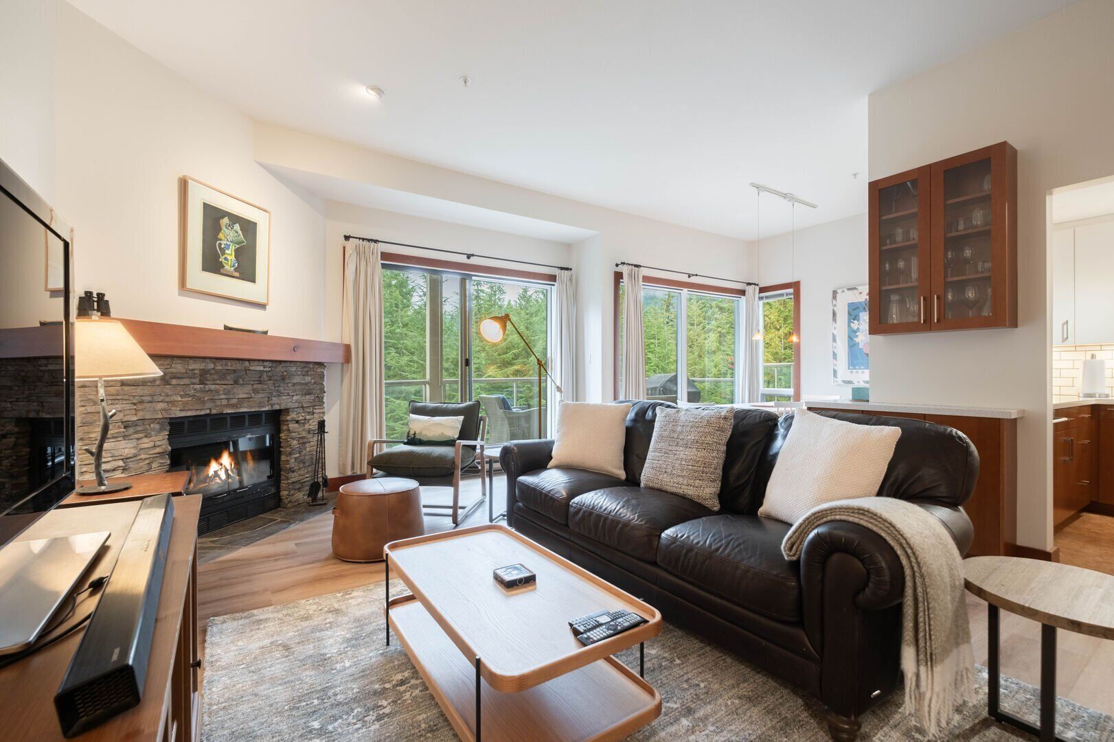 A modern living room with a stone fireplace, leather sofa, and a dining area with a wooden table and bench.