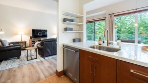 A modern kitchen with a large window, a built-in dishwasher, and a dining area with a black leather sofa and a small table. - Townhome | Smart TVs | Pets | BBQ | Blueberry Hill (Whistler)