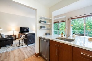 Eine moderne Küche mit großem Fenster, integriertem Geschirrspüler und Essbereich mit schwarzem Ledersofa und kleinem Tisch.