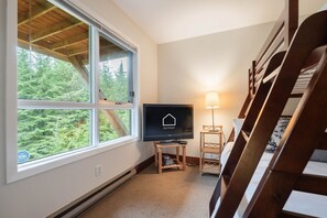 A room with a large window, a television on a stand, a lamp, and a wooden chair. - Townhome | Smart TVs | Pets | BBQ | Blueberry Hill (Whistler)