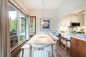 A modern kitchen with a dining area, large windows, and a view of the outdoors. - Townhome | Smart TVs | Pets | BBQ | Blueberry Hill (Whistler)