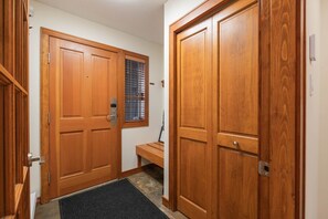 A hallway with wooden double doors, a bench, and a window with blinds. - Townhome | BBQ | Pets | Free Parking | Wifi (Whistler)