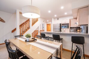 A modern kitchen with stainless steel appliances, a wooden staircase, and a dining area with a large table and chairs. - Townhome BBQ | Smart TV | Private Garage | Wifi (Whistler)