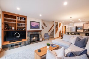 A modern living room with a fireplace, a television, and a staircase leading to a kitchen. - Townhome BBQ | Smart TV | Private Garage | Wifi (Whistler)