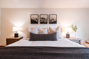 Un lit bien fait, avec un oreiller à rayures, deux tables de chevet avec des lampes et trois tableaux encadrés accrochés au mur.