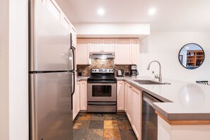 Une cuisine moderne dotée d’appareils électroménagers en acier inoxydable, de meubles de couleur bois clair et d’un grand îlot central avec un évier.