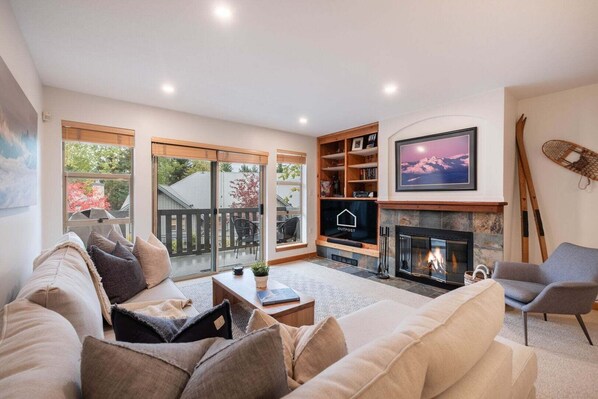 A living room with a fireplace, a television, and a sliding glass door leading to a deck. - Townhome BBQ | Smart TV | Private Garage | Wifi (Whistler)