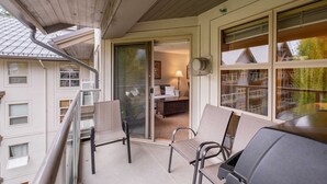 En balkong med en grill, stolar och utsikt över en byggnad med flera fönster och en dörr.
