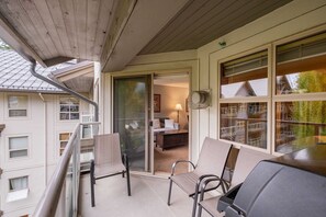A balcony with a grill, chairs, and a view of a building with multiple windows and a door. - Condo | Ski-in/ski-out | Shared pool & hot tub (Whistler)