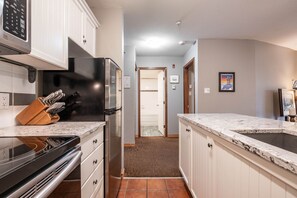 A modern kitchen with white cabinets, a black refrigerator, and a granite countertop. - Condo | Ski-in/ski-out | Shared pool & hot tub (Whistler)