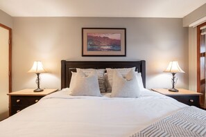 A neatly made bed with a headboard, two bedside tables with lamps, and a framed picture on the wall. - Condo | Ski-in/ski-out | Shared pool & hot tub (Whistler)