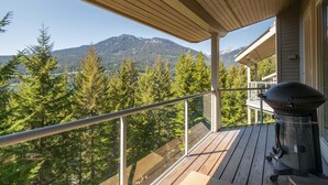 Ein Balkon mit Blick auf einen Wald und Berge, inklusive Grill und einer Holzterrasse.