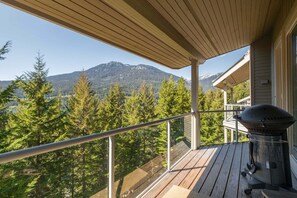 A balcony with a view of a forest and mountains, a grill, and a wooden deck. - Townhome | Pets | BBQ | Free park | SmartTV | Wifi (Whistler)
