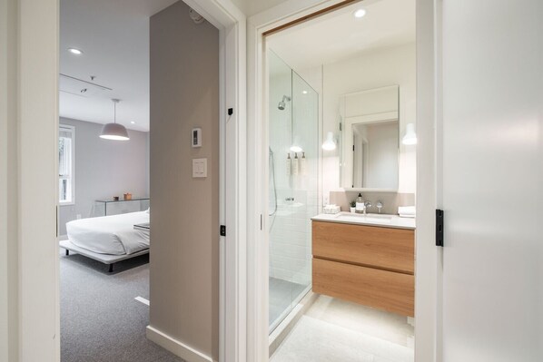 Una habitación de hotel moderna con cama, cabina de ducha de vidrio y tocador de madera con espejo.